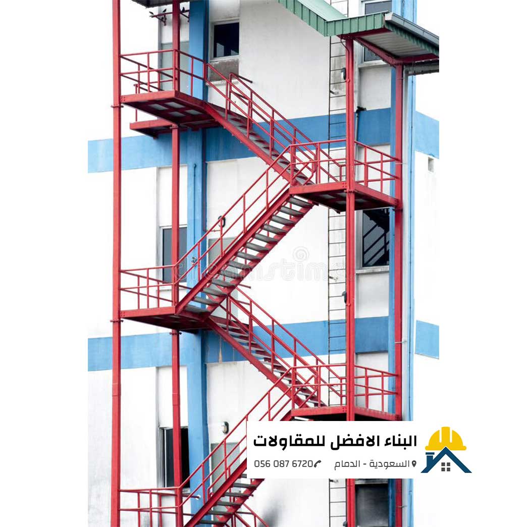 الرئيسية - البناء الافضل للمقاولات سلم ودرج حديد طوارئ خارجي متعدد الطوابق مدهون باللون الأحمر ومثبت على واجهة مبنى باللونين الأبيض والأزرق، مع درابزين حماية وسلم بحري، من تنفيذ مؤسسة البناء الأفضل للمقاولات بالدمام مع الشعار ورقم الاتصال 0560876720.