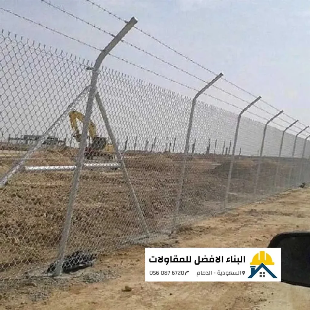 سياج شبكي مجلفن مرتفع ومدعم بأعمدة مائلة يحمي موقع إنشائي وأعمال حفر في الدمام، يعلوه أسلاك شائكة، مع شعار مؤسسة البناء الأفضل للمقاولات.