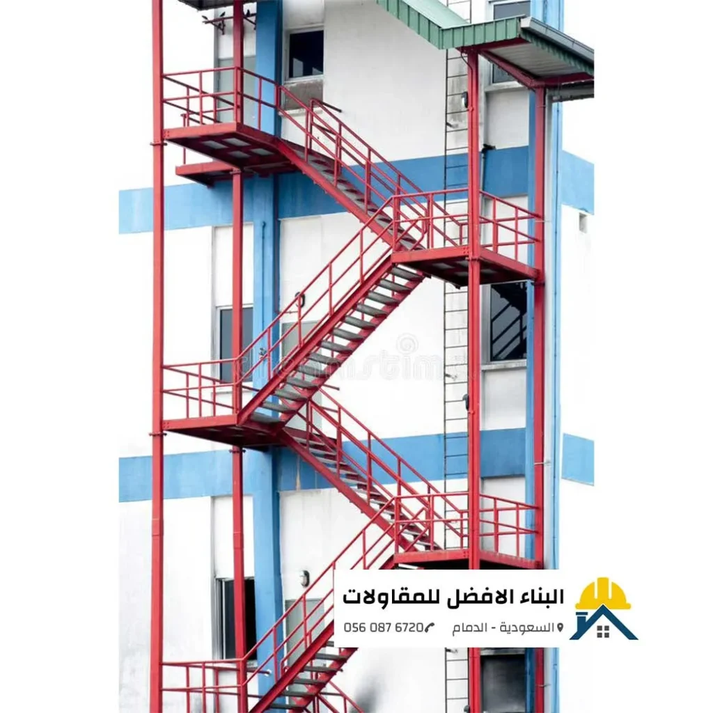 درج حديد خارجي أحمر لأطوارئ ومخارج المباني مثبت على واجهة مبنى تجاري بالدمام، تنفيذ مؤسسة البناء الأفضل للمقاولات.