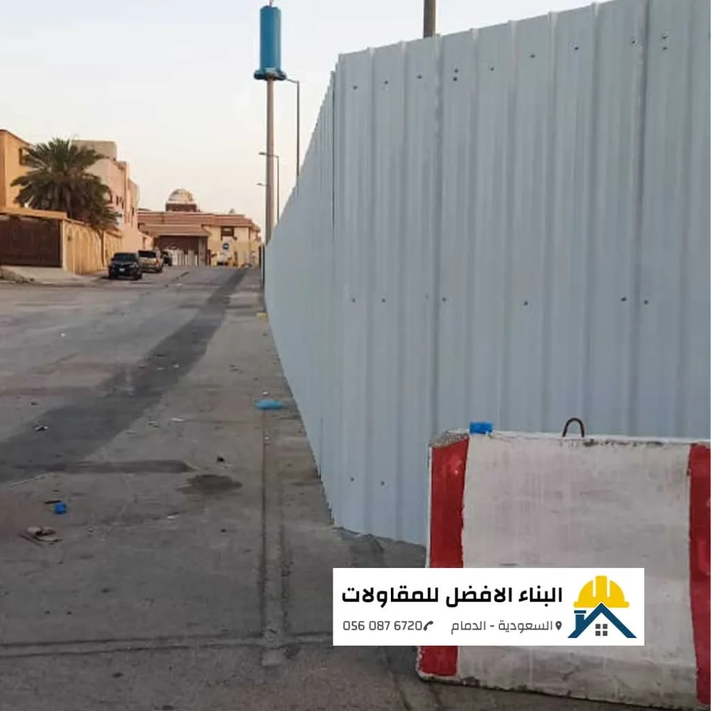 سور تحويشة مؤقت من ألواح الشينكو الأبيض المضلع ممتد على جانب شارع لتسوير موقع إنشائي، مع وجود حاجز خرساني مروري ملون في المقدمة، من تنفيذ مؤسسة البناء الأفضل للمقاولات بالدمام 0560876720.