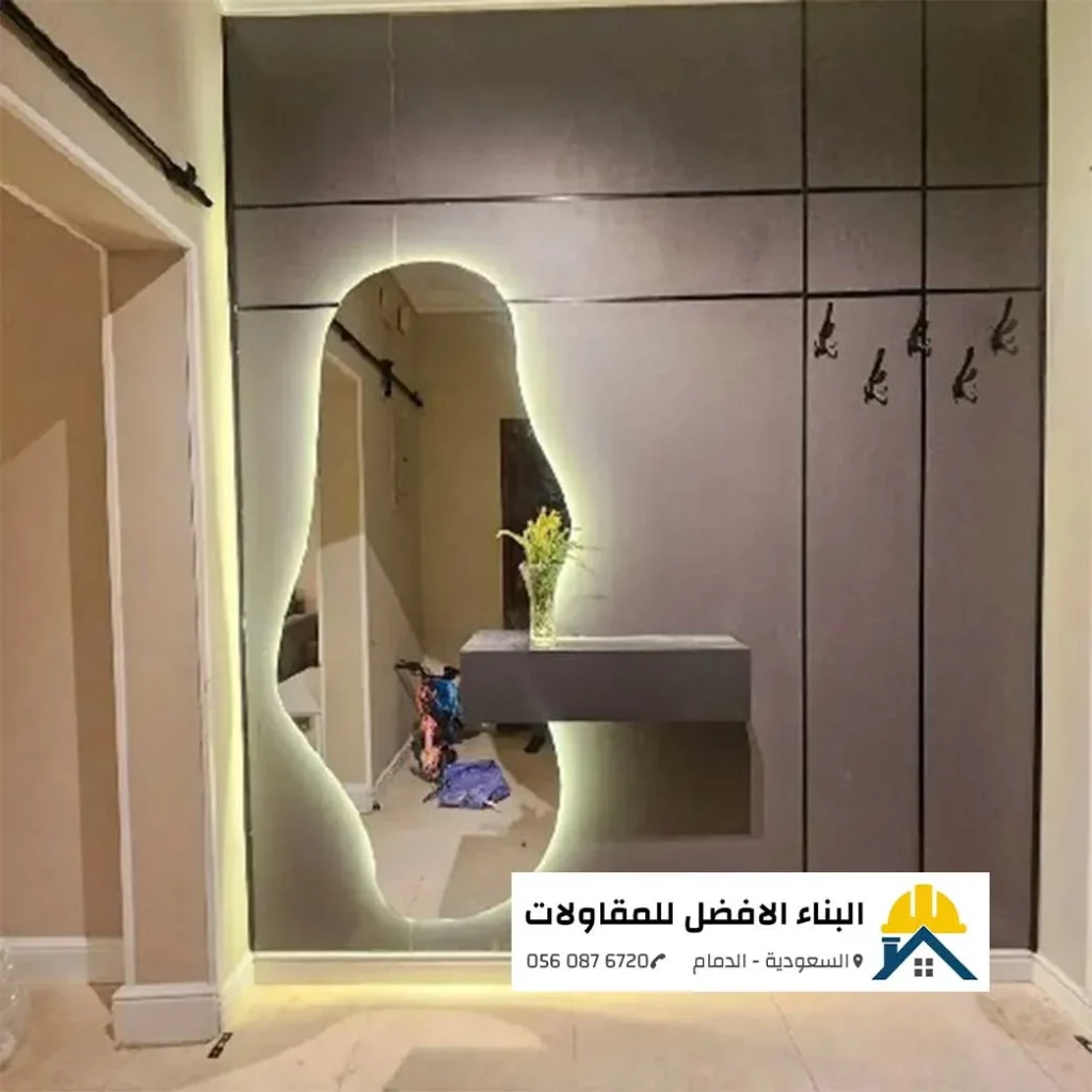 ديكور مدخل داخلي عصري بألواح بديل خشب رمادية ومرآة منحنية مضيئة ورف معلق في الدمام، تنفيذ مؤسسة البناء الأفضل للمقاولات.
