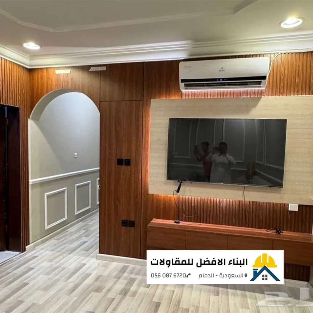 ديكور صالة داخلي بألواح بديل خشب بني وجدار تلفزيون معلق مع إضاءة مخفية وقوس معماري في الدمام، تنفيذ مؤسسة البناء الأفضل للمقاولات.