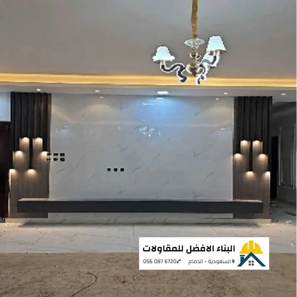 ديكور جدار تلفزيون فاخر يجمع بين بديل الرخام الأبيض وبديل الخشب الجانبي مع إضاءات جدارية في صالة بالدمام، تنفيذ مؤسسة البناء الأفضل للمقاولات.