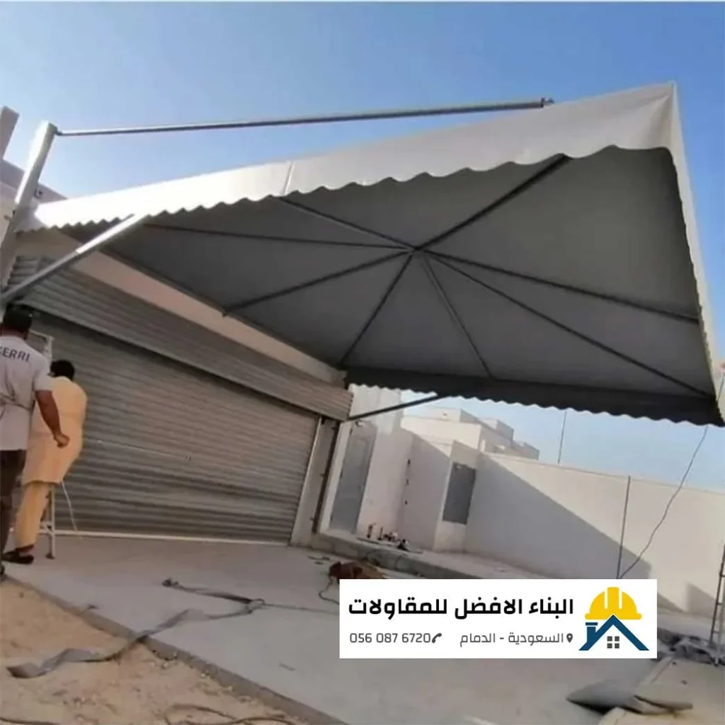 مظلة سيارات معلقة ذات قماش رمادي بتصميم عصري فوق جراج منزلي في الدمام، تنفيذ مؤسسة البناء الأفضل للمقاولات.