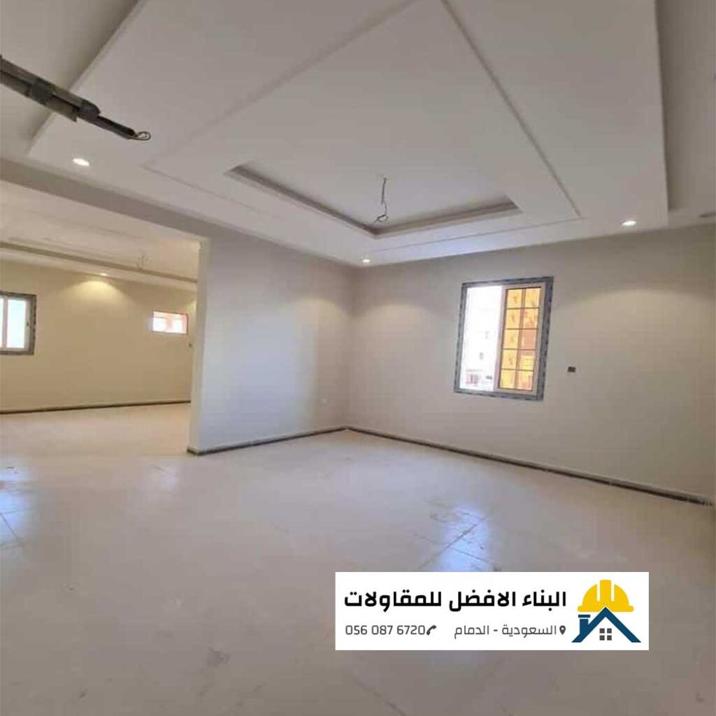 صالة واسعة قيد التشطيب مدهونة بأصباغ داخلية ناعمة باللون الأوف وايت الفاخر مع سقف جبس بورد مودرن مدمج بإضاءة بيت نور وسبوت لايت ونوافذ ألمنيوم، من تنفيذ مؤسسة البناء الأفضل للمقاولات بالدمام مع الشعار ورقم الاتصال 0560876720.