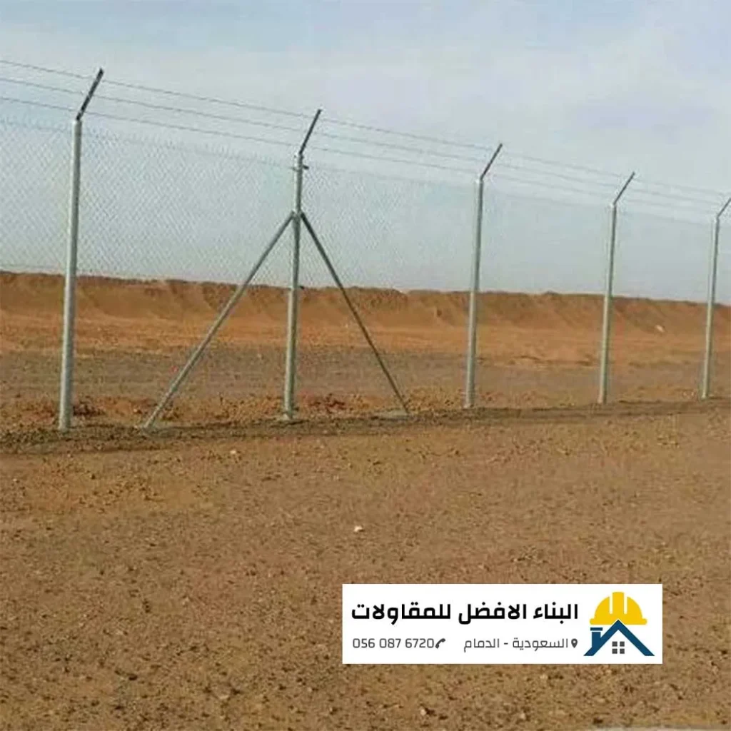 صورة لسياج شبكي مجلفن عالي الجودة مركب فوق كثبان رملية في الدمام، مزود بأسلاك شائكة علوية لزيادة الأمان، ويظهر شعار شركة البناء الأفضل للمقاولات في الزاوية.