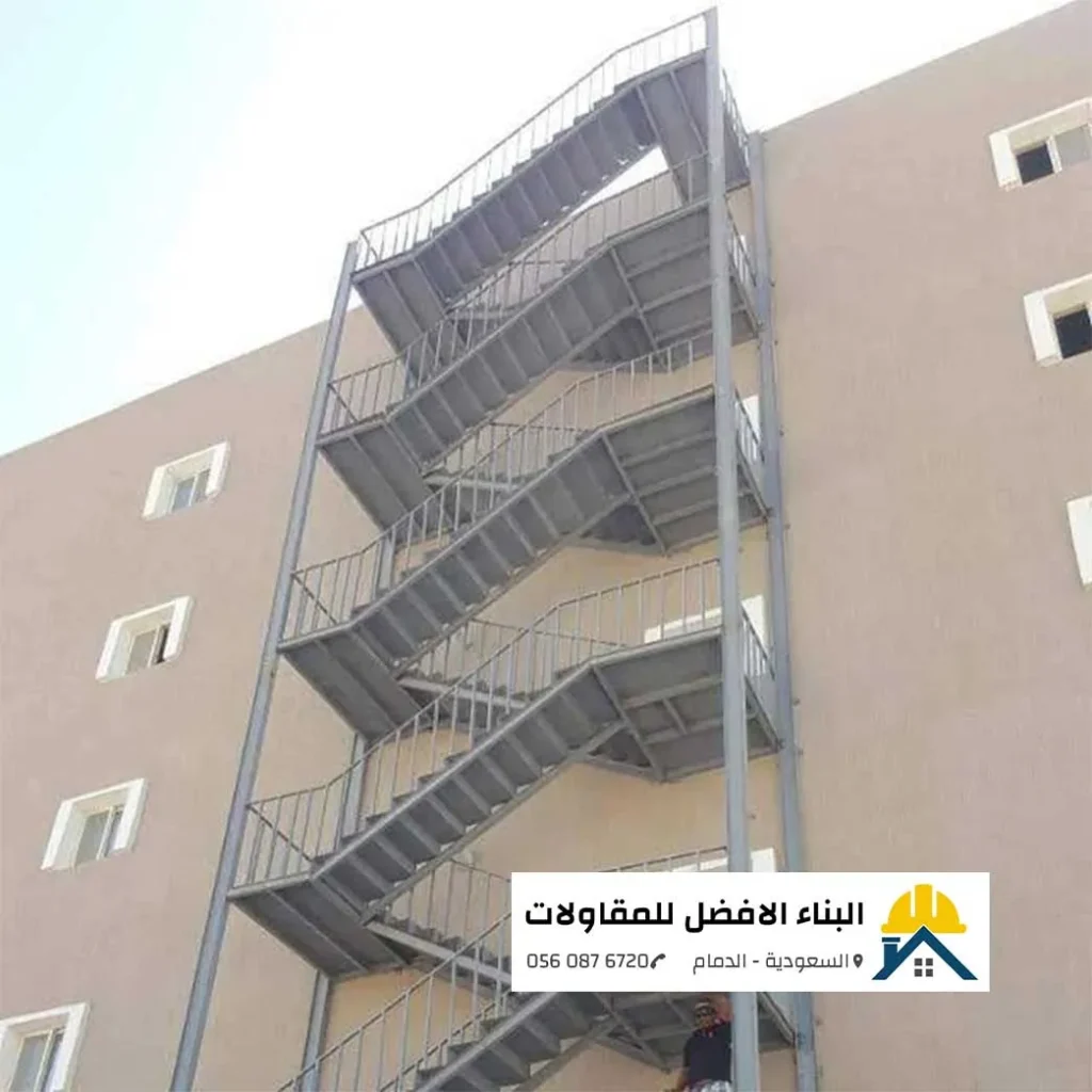 درج حديد خارجي رمادي اللون مخصص لمخارج الطوارئ ومثبت بإحكام على واجهة مبنى بيج بالدمام، تنفيذ مؤسسة البناء الأفضل للمقاولات.